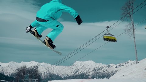Snowboarder demonstrating a jump in flight. Winter outdoor activities and snowboard training in special clothing. Incredible views of the sky and mountains. Concept of extreme sports and leisure