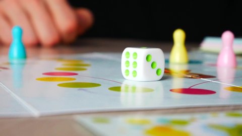 A man rolls a dice and moves a piece playing a board game