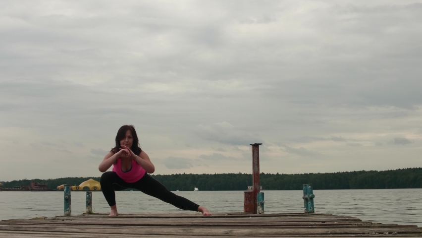 Side view of woman in pink tank and black tights doing stretch before excercises