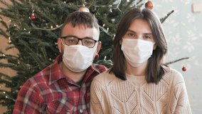 Young couple meet Christmas covid-19 pandemic. Husband and wife wearing protective medical masks and greeting in a house with Christmas decorations. New normal Christmas holiday concept, video call 