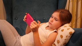 Little child girl lie in a chair hold use smartphone playing phone game application and watch social media