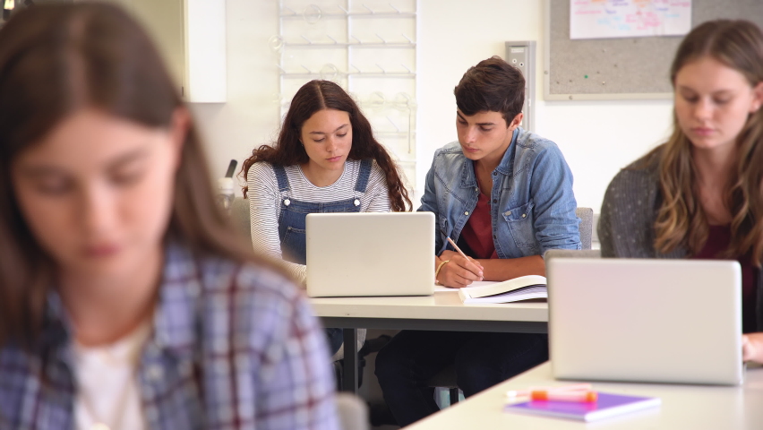 College students sitting together at desk and using laptop during computer lesson. Young man and casual girl working together on laptop in high school library or classroom. Royalty-Free Stock Footage #1064040598