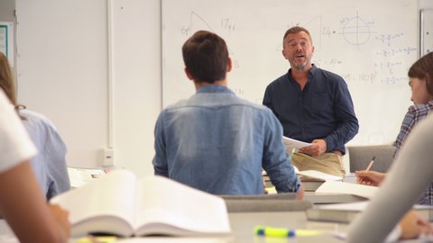 Professor pointing at college student with hand raised. Student raising a hand with a question for the teacher. Lecturer teaching in class while girl have a question to do during a math lesson.