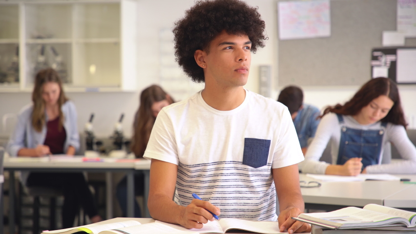 Portrait of contemplative young man during exam at high school, copy space. Smiling college student doing homework in class while looking away. Happy african young man preparing for exam in university | Shutterstock HD Video #1064040616