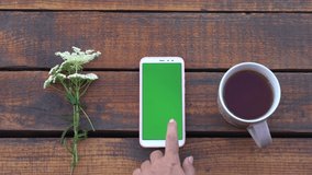 Closeup top view flatlay 4k video of modern smartphone laying on brown wooden surface. Screen of device with empty blank green color. - Powered by Shutterstock - Get 15% off with code: PIKWIZARD15