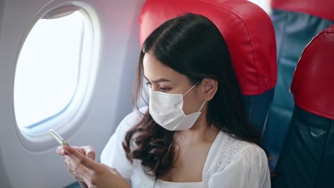 A young woman wearing face mask is using smartphone onboard, New normal travel after covid-19 pandemic concept	