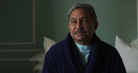 Senior mixed race man sitting up in bed looking away. self isolation retirement lifestyle at home during coronavirus covid 19 pandemic.