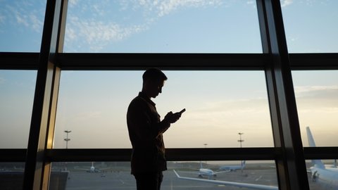 man with a phone stops in front of an airport window with a view of planes.