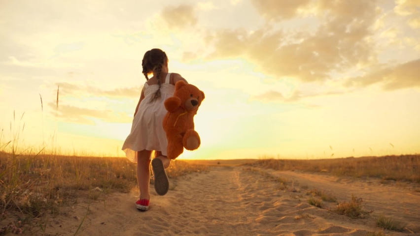 Little girl with a toy teddy bear in park. Cute girl with a teddy bear in a green field. Lonely girl with a toy teddy bear in park in green field.Teddy bear in the hands of a girl in the park Royalty-Free Stock Footage #1064059012
