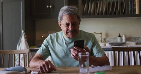 Senior mixed race man having video chat on smartphone in kitchen. self isolation retirement lifestyle at home during coronavirus covid 19 pandemic.