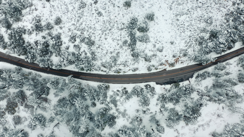 Aerial view of mountain road bending in forest. Aerial of car parked in winter wonderland. Vacation getaway, top view of white frozen wanderlust travel destination. North nature landscape in winter 4K