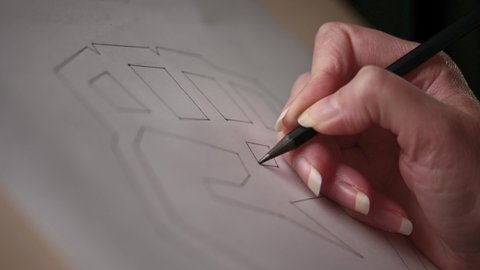 The artist makes a sketch on a piece of paper. Close-up of a hand with a pencil.