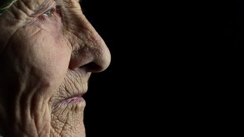 An aged mother. Old age concept. Aged parents and caring for them. Grandma in the dark. Eyes.Old grandmother in profile on a dark background. Wrinkles on the old face of the grandmother.