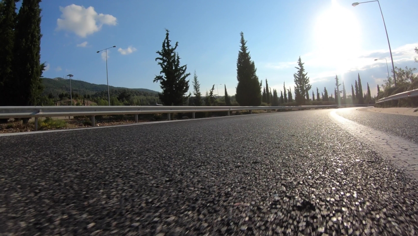 Fast moving POV video of asphalt road with clear blue skies taken by stabilised camera attached to motorcycle as seen from asphalt road perspective, Attica, Greece | Shutterstock HD Video #1064068549