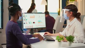 Office manager explaining to black colleague financial startegy pointing graphs on desktop wearing face masks and visors. Multiethnic team working in company with new normal respecting social distance - Powered by Shutterstock - Get 15% off with code: PIKWIZARD15