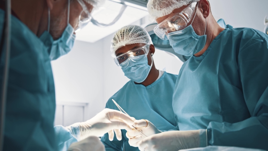 Diverse surgical corporate staff perform operation with chief surgeon doctor in hospital operating room. Collaboration. Surgery concept. Royalty-Free Stock Footage #1064071789