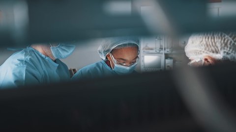 Diverse mixed-race surgeon afro-american woman with several doctors performing medical surgery operation in operating room modern hospital collaborating.