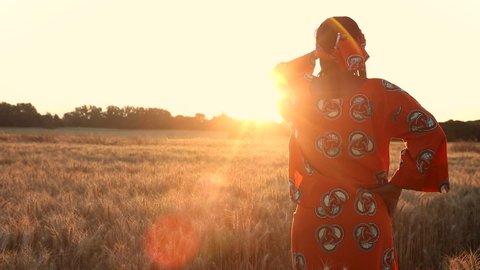 HD Video clip of African woman farmer in traditional clothes standing in a field of crops, wheat or barley, in Africa at sunset or sunrise