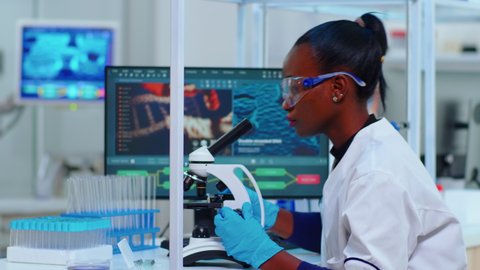 African woman biochemist using microscope in modern equipped laboratory. Black scientist doctor working with various bacteria, tissue, blood samples, pharmaceutical research for antibiotics