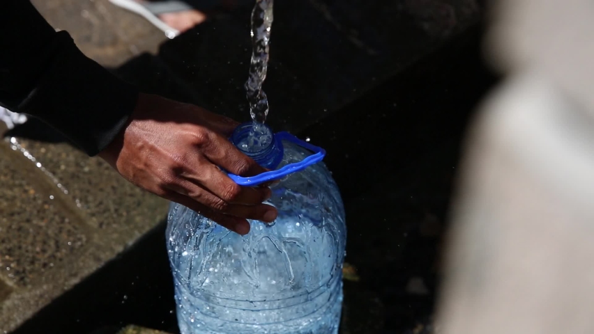 Collecting natural spring water with 5 litre plastic water bottle from a  natural spring in water crisis and massive drought in Africa Royalty-Free Stock Footage #1064083525