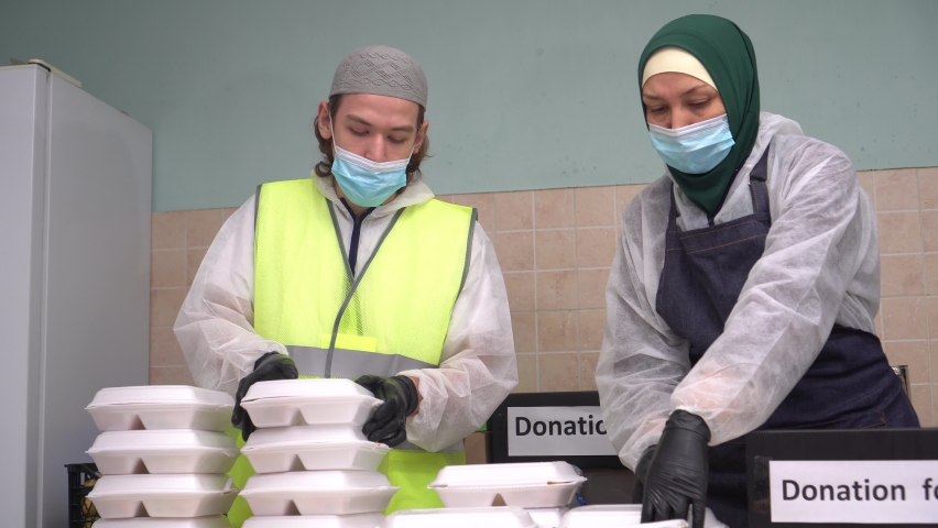 Muslim volunteers pack free hot meals in take out boxes. Muslim Soup Kitchen. Free groceries, Charity on Ramadan Royalty-Free Stock Footage #1064084464