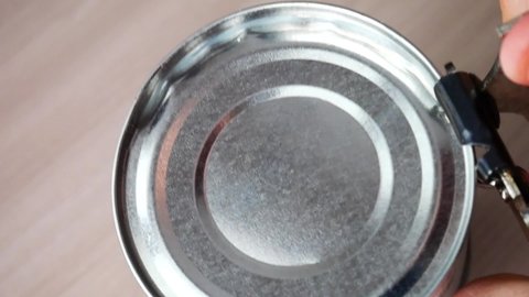 Someone opens a tin can with a can opener close-up