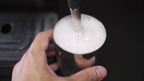 Barista steaming milk in frothing pitcher in slow motion. steam wand heating milk.