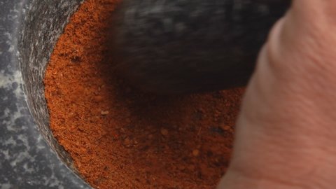 Close-up of the pestle grinding a mix of spices, peppers and sea salt in the grey stone mortar