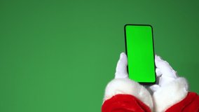 The hand of modern Santa Claus is holding a smartphone. The smartphone has a chroma key. Santa is shopping online. The concept of a modern man.