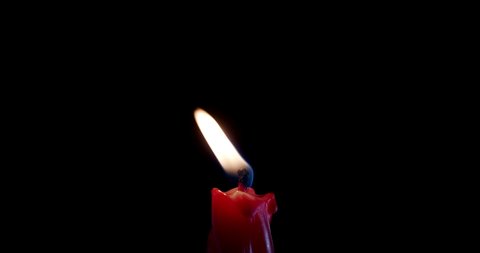 A single red candle burning. Isolated candle burning with dark background. Red paraffin candle with yellow shades burns on a black background. Background or illustration of remembrance or celebration.