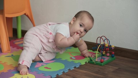 infant, childhood concept - happy funny toddler kid 8 month baby girl sit lick playing Wooden and Wired Bead Maze Abacus game on mat. chubby awake newborn crawl on floor in playroom indoors at home