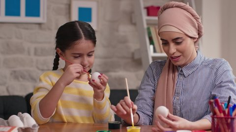 Easter, family, holiday and children concept. A mother and daughter in a turban are painting eggs. A happy family is preparing for Easter.
