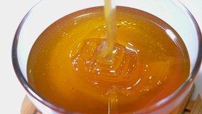 Honey pouring honey in glass bowl. Close-up. Healthy organic Thick honey dipping from the honey spoon, closeup. 4K UHD video footage. Slow motion