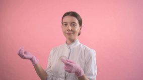 The girl works in a beauty salon. Hands in medical pink gloves hold dental floss. Pink background.