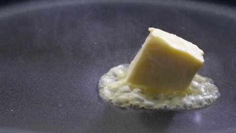 Cube of butter melting sizzling. Butter melting sizzling in frying pan on stove. Close up.