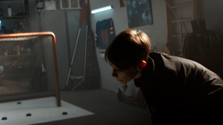 Kid boy hockey player practicing shots inside a covered garage at home. Shot with 2x anamorphic lens