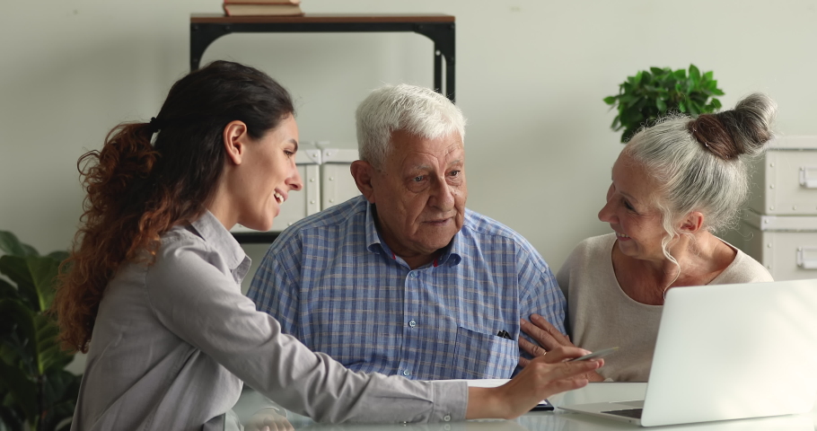 Touristic agency worker explain showing on laptop travel offers tell about tour prices to happy older couple in office. Insurer woman presents offer medical insurance services to aged spouses concept | Shutterstock HD Video #1064112298