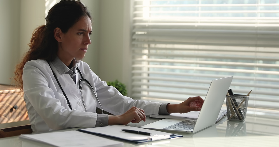 Female doctor in white uniform sit at desk read news on laptop learn information statistics of coronavirus infected patients feels stressed, problems at work, professional failure, dismissal concept Royalty-Free Stock Footage #1064112820