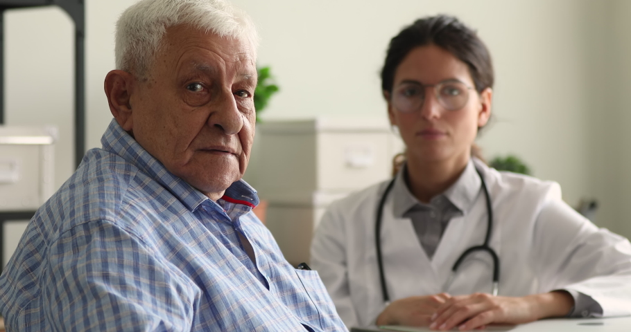 Older male patient and doctor on background smile looking at camera sit in clinic office. Portrait of satisfied hospital client, reliable high quality professional eldercare, medical insurance concept Royalty-Free Stock Footage #1064113021