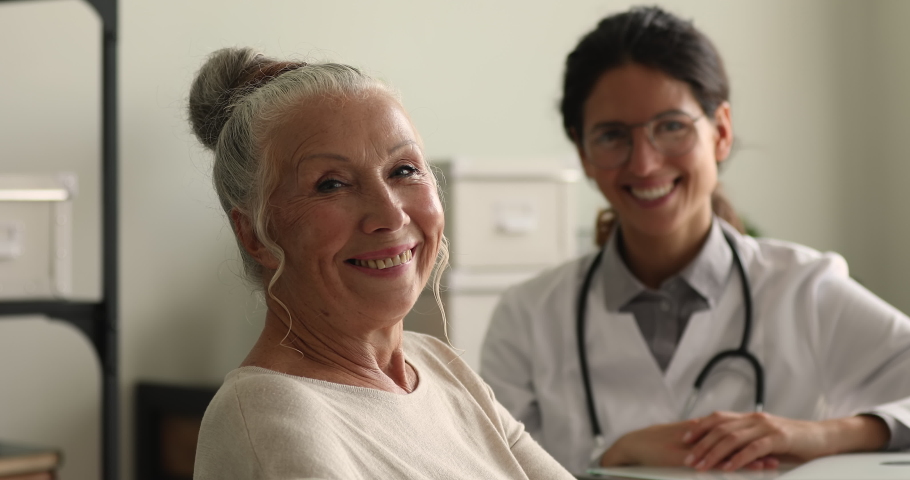 Seated in clinic office 70s female client and general practitioner doctor on background smile look at camera. Portrait of satisfied with treatment results, medicare patient, medical insurance concept | Shutterstock HD Video #1064113024