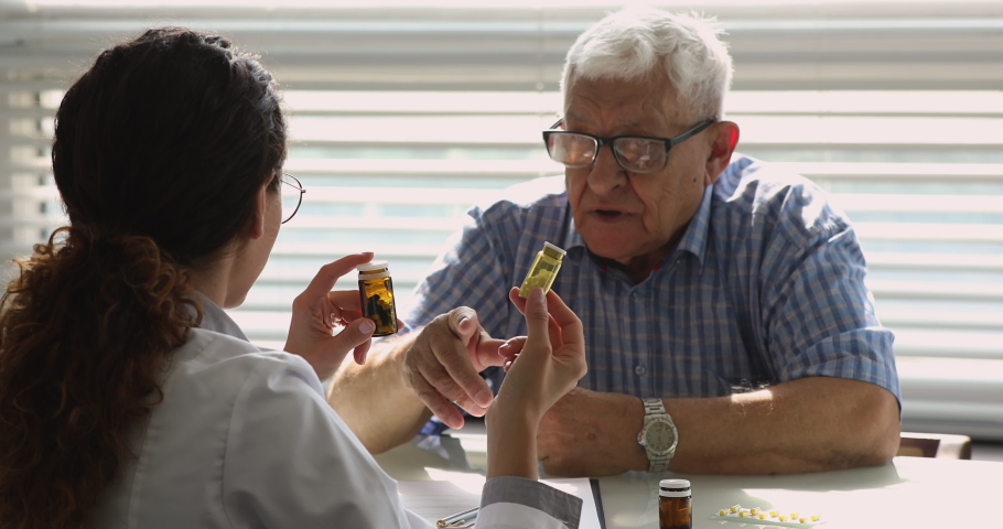 Female doctor talk to old unhealthy male patient during visit in private clinic, show bottles with meds explain prescription, give professional consultation. Chronic disease treatment pharmacy concept Royalty-Free Stock Footage #1064113147