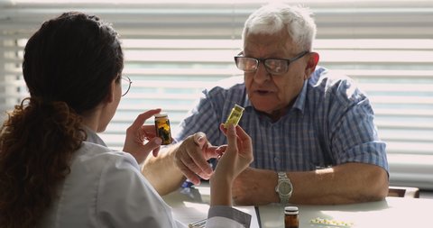 Female doctor talk to old unhealthy male patient during visit in private clinic, show bottles with meds explain prescription, give professional consultation. Chronic disease treatment pharmacy concept