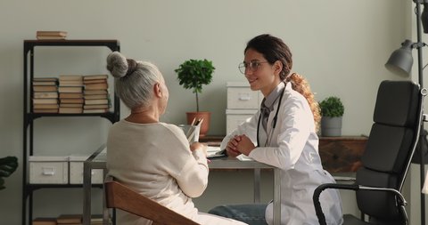 Young doctor in white coat talk to 65s female patient during visit in clinic, explain further diagnostics, general check up, disease treatment. Health exam, medical insurance for older people concept