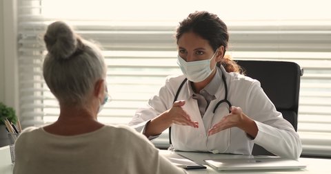 Aged patient receive consultation in medical centre concept. Therapist wear disposable surgical mask talk to older female during visit, give advice, tell about general checkup, health analysis results