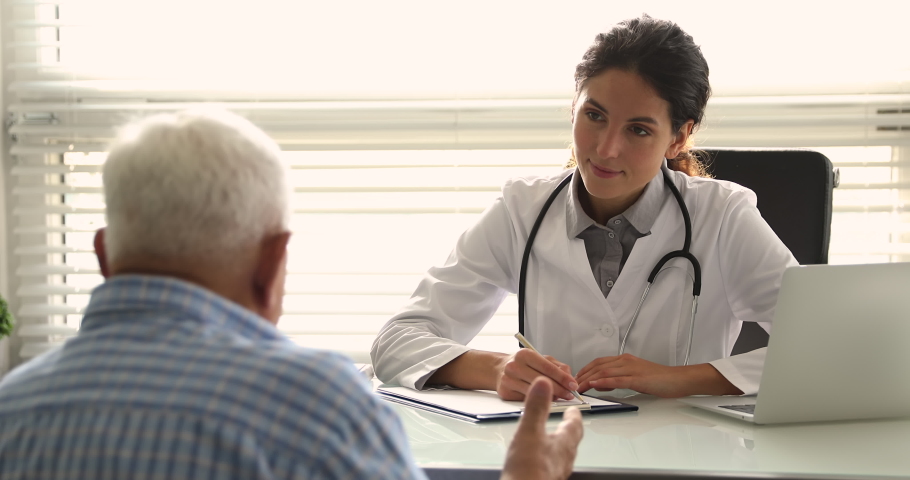 Young woman doctor in white uniform and stethoscope on neck talk to older patient, discuss health concerns writes complaints, fill medical form. General check up, healthcare, medical insurance concept Royalty-Free Stock Footage #1064113504