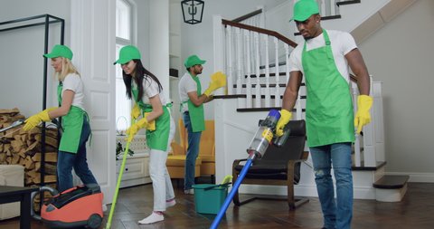 An attractive positive skilled young international group of workers of cleaning service in uniforms cleaning up contemporary apartment,service industries concept.