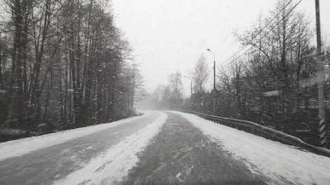 View through the windshield on the highway in winter along which the car is driving in heavy snow and wind in Russia.