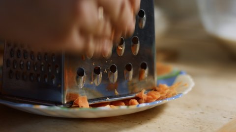 Female hand rubbing carrots on a grater in the home kitchen. 4K video