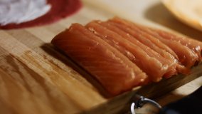 Thin tasty colorful pancakes. Close-up of woman's hand laying salmon slices as filling on red pancake anointed with creamy cheese on a wooden board. Rolling the pancake. Slowmotion dream effect. 4K