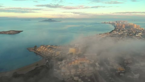 Aerial drone point of view La Manga del Mar Menor spanish touristic resort city during misty weather in early morning, residential buildings rooftops and Mediterranean Seascape. Murcia, south of Spain